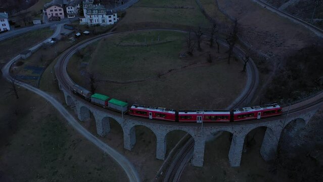 Train on Brusio Spiral Viaduct in Switzerland in the Evening. Bernina Railway. Swiss Alps. Aerial View. Drone Flies Backwards and Upwards
