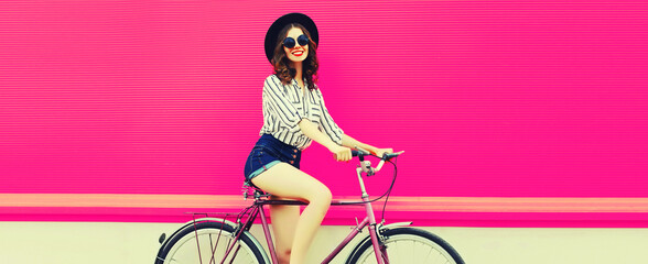 Summer colorful portrait of happy smiling young woman with bicycle in the city on pink background