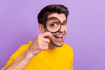 Portrait of cheerful laughing man using magnifying glass find investigation isolated on purple...