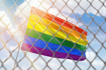 A steel mesh against the background of a blue sky and a flagpole with flag of lgbt pride
