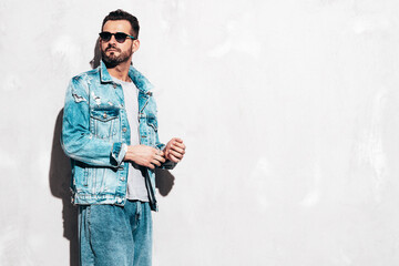 Portrait of handsome confident stylish hipster lambersexual model. Sexy man dressed in jeans jacket. Fashion male isolated on grey wall in studio. In sunglasses