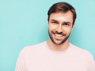 Closeup portrait of handsome smiling stylish hipster lambersexual model. Sexy man dressed in pink T-shirt and trousers. Fashion male isolated on blue wall in studio