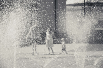 Defocused blurred black and white photo. Mother father and little kid f on sunny day walking in park.  The fountain water spray drops. Dancing floor groundwater dry fountain.Happy family entertainment