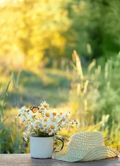 Rolgordijnen kamille bloemen in witte kop en gevlochten hoed op tafel in de tuin, zonnige natuurlijke abstracte achtergrond. zomerseizoen. samenstelling. ontspanning, harmonie sfeer © Ju_see