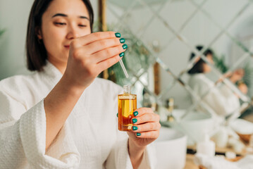 Facial Skincare. Happy Korean asian woman applying Facial serum using dropper standing in modern bathroom.