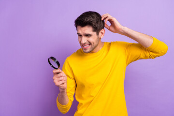 Photo of young negative mood man scratch head can't find something using loupe isolated on violet...