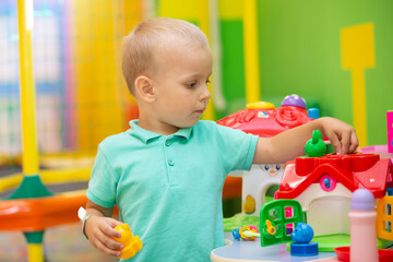 A little boy plays with a lot of colorful plastic toys indoors.