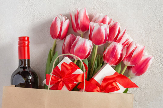 Mother's Day or Women's Day, birthday, wedding congratulation. Spring tulips with a gift box and a bottle of wine in a paper bag.