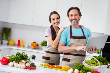 Photo of two positive idyllic partners hug toothy smile hold wireless netbook kitchen indoors