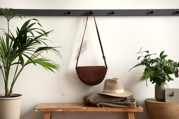The stylish composition of cosy entryway with wooden bench, coffee table, bag hanger and personal...