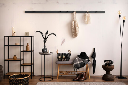 The stylish composition of cosy entryway with grey bench, black consola, hanger and lamp. Beige wall. Home decor. Template.