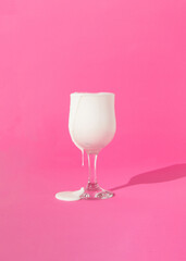 Whipped cream is overflowing and dipping from wine glass on pink background. Minimal sucess and celebration concept. Glass overflowing concept.