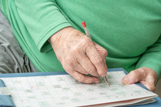 Wrinkled Hand Of An Old Senior Man Or Woman Solving Crossword Puzzle