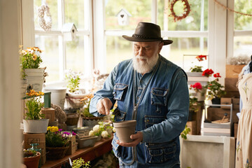 Senior man in cowboy hat planting flowers in his shop