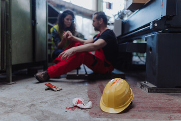 Woman is helping her colleague after accident in factory. First aid support on workplace concept.