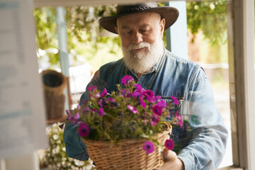 Old smiling male florist looking after pot plants
