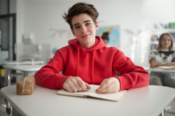 College student sitting in school-desk and looking in camera.