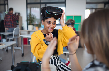 Happy student wearing virtual reality goggles at school in computer science class, playing with her...