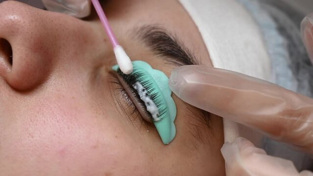 The master removes the composition for lamination from the client's eyelashes with a cotton swab. Eyelash perm procedure.