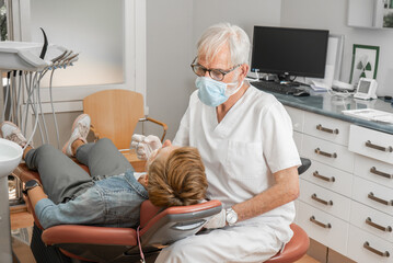 Mature experienced male doctor in glasses and face mask performs a regular examination of the patient. Doctoral practice. Patient healthcare