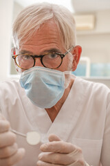 Close Up portrait of a mature experienced male doctor in glasses and face mask with dentist tools.