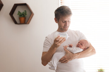 Father holding and feeding his newborn son with milk bottle at home.