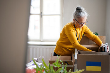 Senior volunteer woman packing box with Humanitarian aid for Ukrainian refugees in office