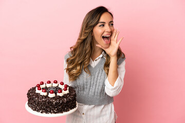 Young woman holding birthday cake over isolated pink background shouting with mouth wide open to...