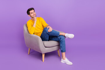 Fototapeta na wymiar Full body image of young positive dreaming man sit armchair relaxing brainstorming isolated on purple color background