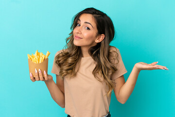 Young woman holding fried chips over isolated background having doubts while raising hands