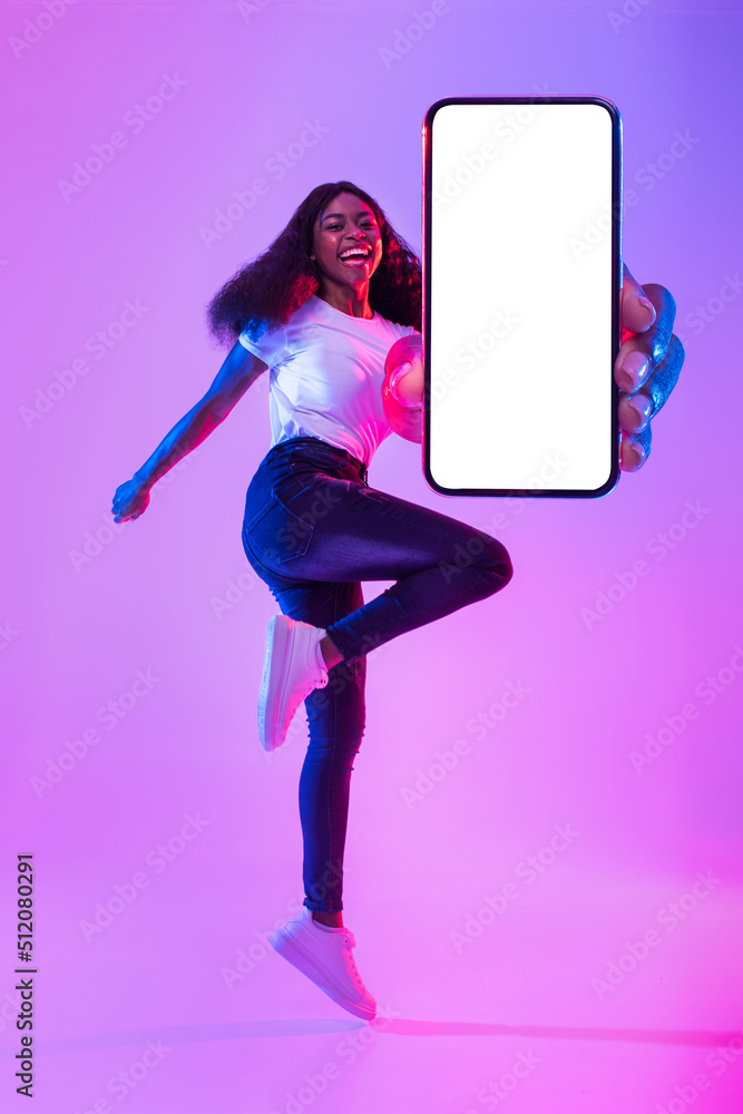 Poster black lady showing smartphone with empty screen, jumping up in air, offering space for mobile app in