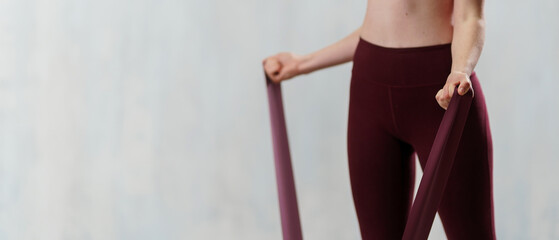 Close-up of sports woman in fashion sportswear exercising with elastic band stretch over greay background.