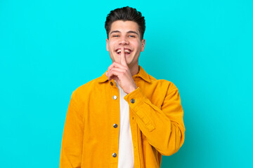 Fototapeta premium Young handsome caucasian man isolated on blue bakcground showing a sign of silence gesture putting finger in mouth