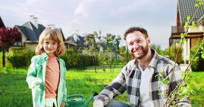 Happy joyful father and cute small son working in garden together and giving high five to each other in gloves. Portrait shot. Little kid with dad planting trees in orchard. Outside.