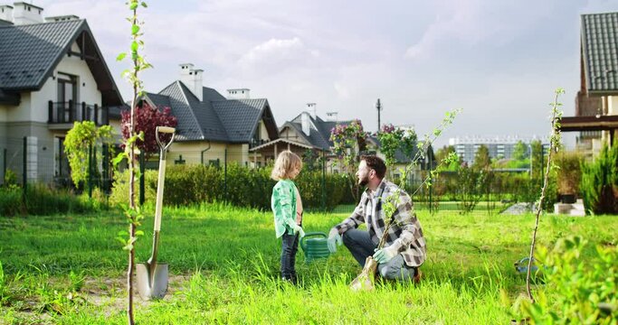Happy cheerful father and cute small son working in garden together and giving high five to each other. Little kid with dad planting trees in orchard. Summer work at village house. Outdoor.