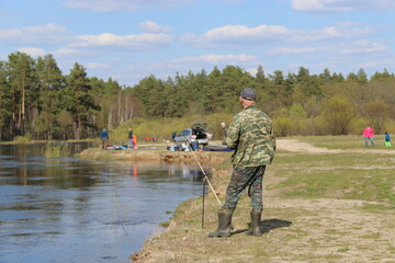 A man is fishing on the river. Fisherman on the shore, camouflage clothing. Beach, river bank