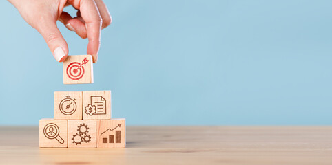 Female hand putting wooden cube block stacking with icon on blue background. Concept of business strategy and action plan