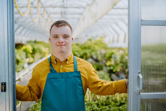 Young employee with Down syndrome working in garden centre, looking at camera and standing in door of greenhouse