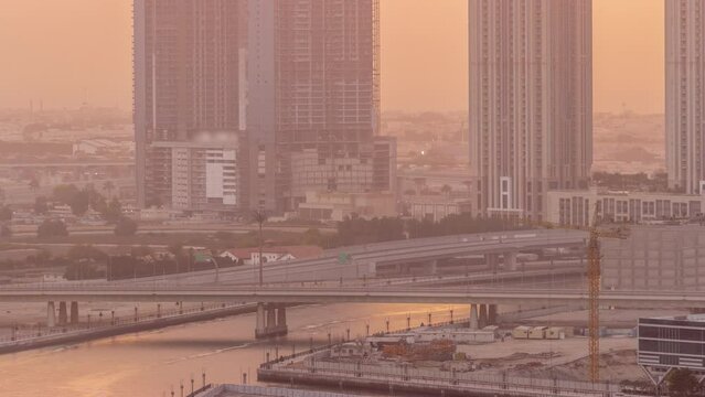 Cityscape skyscrapers of Dubai Business Bay with bridge over water canal and sunset sky aerial timelapse. Modern skyline with towers under construction and waterfront. A center of international