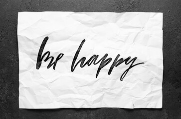 Be happy. Lettering on crumpled white paper. Handwritten text. Inspirational quotes.