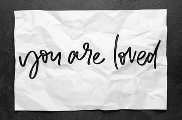You are loved. Lettering on crumpled white paper. Handwritten text. Inspirational quotes.