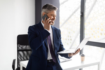 Middle Aged Businessman Talking On Cellphone And Using Laptop At Office