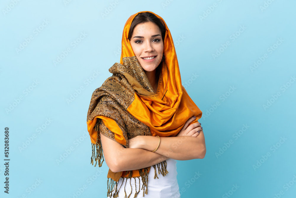 Poster Young Moroccan woman with traditional costume isolated on blue background with arms crossed and looking forward