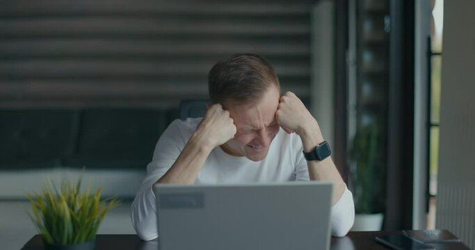 Frustrated young man sitting in front of his laptop after seeing big mistake he lost