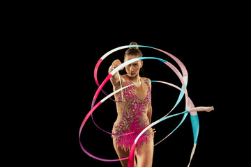 One young sportive girl, rhythmic gymnastics artist performing with ribbon isolated on dark...