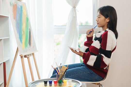 The art concept, Asian female artist sitting front of canvas and thinking to create about artwork