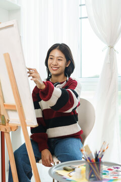 The art concept, Asian female artist in sweater use paint brush to painting on canvas in art studio