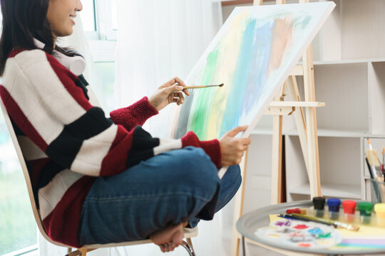 The art concept, Asian female artist sitting on the chair and holding canvas to painting artwork