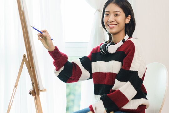 The art concept, Asian female artist in sweater with headphone to painting on canvas in art studio