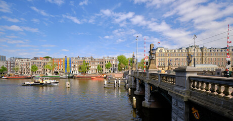 Amsterdam, Netherlands, 11 May 2022 - Panoramic.View of bridge spanning the Amstel river with passenger boats and the city skyline. Blue skies in spring sunshine.